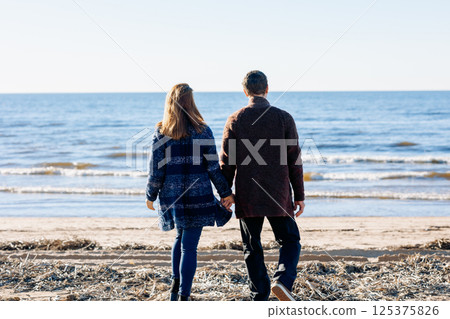 Loving couple walks on beach along sea on sunny autumn day. Weekend and lifestyle concept. Back view. High quality photo Loving couple walks on beach along sea on sunny autumn day. Weekend and lifestyle concept. Back view. High quality photo 125375826