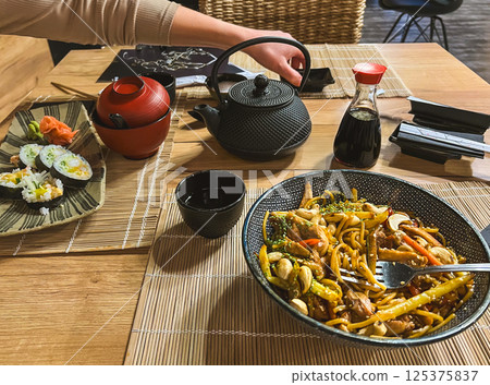 Spaghetti with chicken, mushrooms and sesame seeds on a plate in a asian food restaurant with teapot and chopsticks 125375837