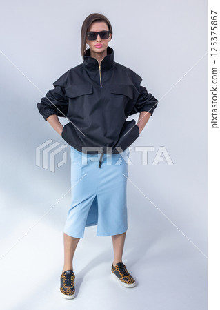 Elegant woman in black windbreaker jacket and light blue skirt on white background. Fashionable female style. Studio photography. Vertical photo. High quality photo 125375867