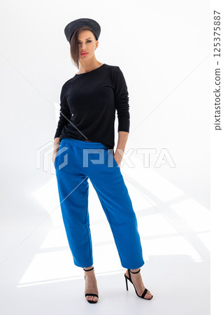 Elegant woman in black windbreaker jacket, blue pants and nautical hat on white background. Fashionable female in ocean French style. tudio photography. Vertical photo. High quality photo 125375887