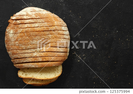 Sliced homemade sourdough rye bread with rye flour on black textured background. Top view or flat-lay 125375994