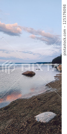 Spring landscape. Panoramic view of beautiful dawn on bay. Cumulus clouds over water in bright light. Ice, snow and rocks on coastline. Rising rays of sun are reflected in sea. Vertical photo. Spring landscape. Panoramic view of beautiful dawn on bay. Cumulus clouds over water in bright light. Ice, snow and rocks on coastline. Rising rays of sun are reflected in sea. Vertical photo. 125376098