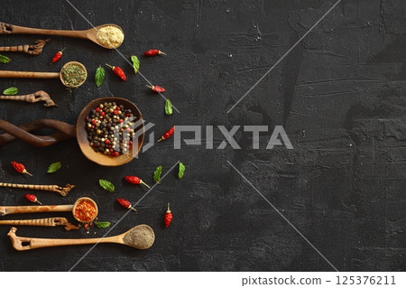 Different kind of spices on a black stone. Oriental spices in spoons, peppers, curry powder, herbs on black Different kind of spices on a black stone. Oriental spices in spoons, peppers, curry powder, herbs on black 125376211