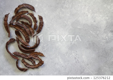 Carob. Healthy organic sweet carob pods on gray wooden background closeup. 125376212