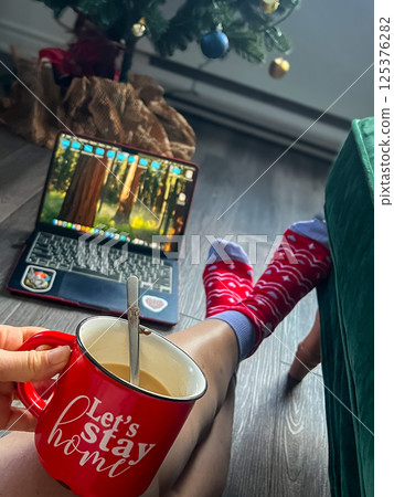 Cup of coffee in the hands of a woman on the background of a laptop. Stay at home concept 125376282