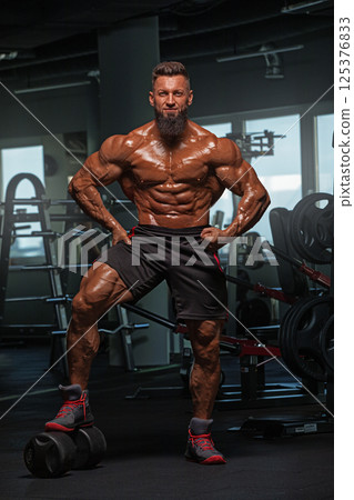 muscular individual showcases his physique in fitness center. He stands confidently arms flexed highlighting his toned muscles and strong stance. muscular individual showcases his physique in fitness center. He stands confidently arms flexed highlighting his toned muscles and strong stance. 125376833