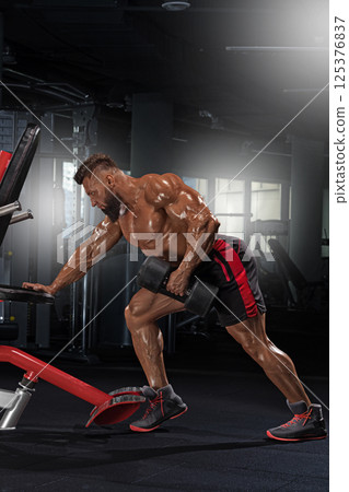 muscular individual engages in weightlifting well equipped gym. Focused on building strength he performs exercise dumbbells showcasing determination and dedication. 125376837