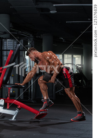 athletic man is engaged in strength training focusing on his upper body using gym equipment. well lit gym features various fitness tools enhancing workout ambiance. 125376839