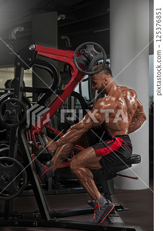 bodybuilder performs seated machine workout targeting back muscles in contemporary gym setting. vibrant environment enhances energy of workout session. bodybuilder performs seated machine workout targeting back muscles in contemporary gym setting. vibrant environment enhances energy of workout session. 125376851