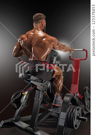 muscular male athlete focuses on strength training using machine designed for back exercises. gym is well equipped showcasing various weights and equipment. 125376853