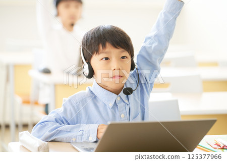 Elementary school boy raising his hand with a laptop open Elementary school boy raising his hand with a laptop open 125377966