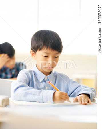 Elementary school boy writing with concentration | Serious expression as he concentrates on his studies Elementary school boy writing with concentration | Serious expression as he concentrates on his studies 125378073
