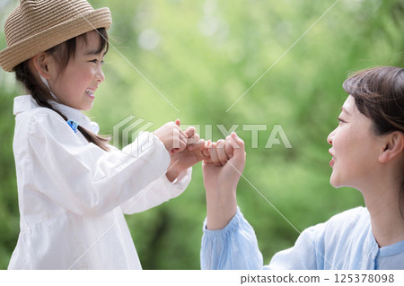 一個孩子和一個大人在一片新綠的背景下勾起小指許下承諾——象徵未來、希望以及許下和遵守承諾 125378098