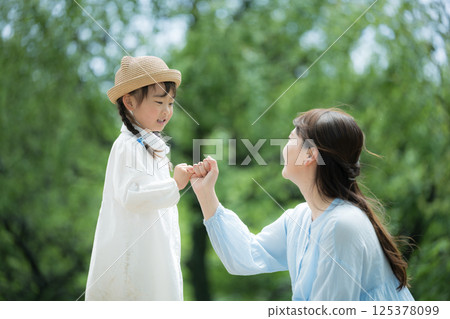 一個孩子和一個大人在一片新綠的背景下勾起小指許下承諾——象徵未來、希望以及許下和遵守承諾 125378099