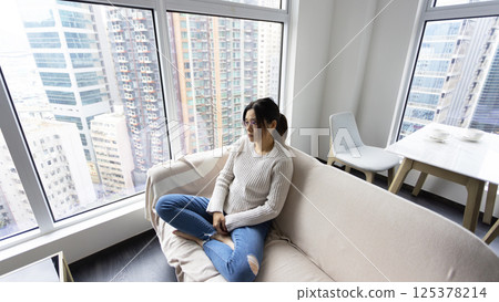 woman wear glasses sit on the sofa and feel stressed, full body shot with house estate background 125378214