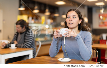 Portrait of girl with cup in hands drinking coffee in coffee shop indoors Portrait of girl with cup in hands drinking coffee in coffee shop indoors 125378705