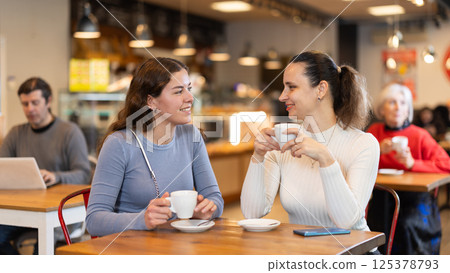 Girlfriends are chatting happily with each other while sitting at table in a cafe and drinking tea Girlfriends are chatting happily with each other while sitting at table in a cafe and drinking tea 125378793