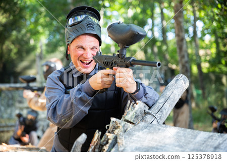 Excited man paintball player aiming with paintball gun and shooting 125378918