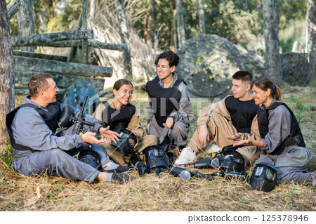 Group of male and female paintball players sitting on ground and talking Group of male and female paintball players sitting on ground and talking 125378946