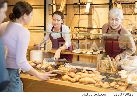Smiling female bakers in maroon aprons working behind counter 125379025