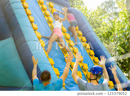 Cheerful girl climbing on inflatable slide with wooden poles Cheerful girl climbing on inflatable slide with wooden poles 125379052