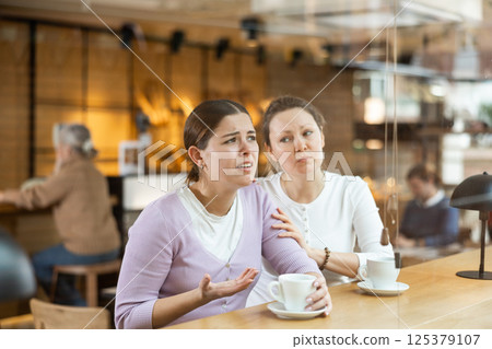 Distressed young woman telling her story to her friend in cozy cafe Distressed young woman telling her story to her friend in cozy cafe 125379107