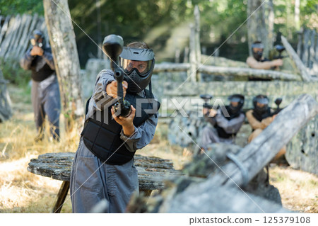 Woman in protective clothes and helmet aiming with paintball marker 125379108