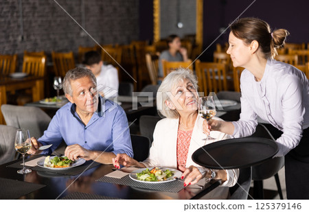 Female waiter serving wine to elderly couple in restaurant 125379146