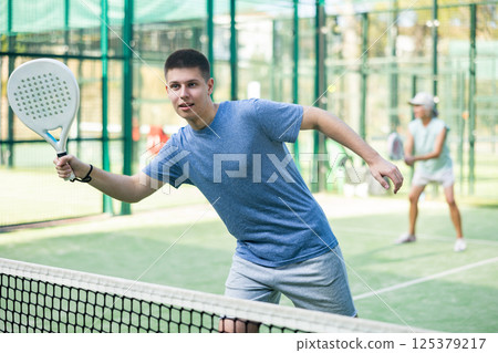 Sporty young guy playing padel on open court in summer Sporty young guy playing padel on open court in summer 125379217