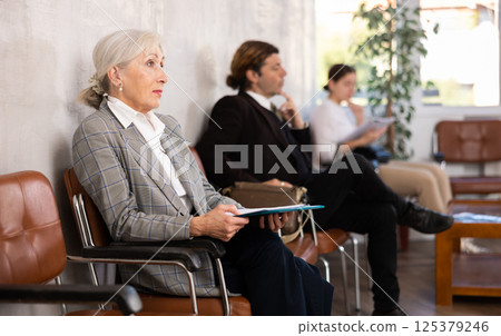 Elderly woman in suit with folder of documents sits on chair 125379246