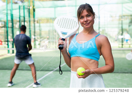 Positive girl looking at camera while playing padel at court 125379248
