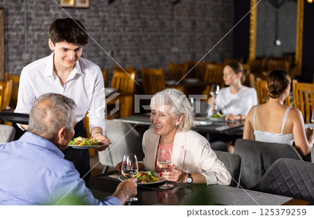 Restaurateur guy serves customers elderly spouses plate with dinner order 125379259