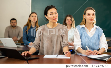 Students writing in notebook and typing on laptop during class in classroom 125379288