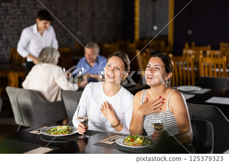 Two joyful smiling female friends having nice conversation in cafe during leisurely hearty dinner 125379323