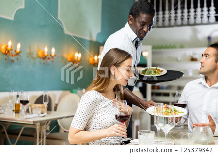 African american waiter bringing ordered dishes to couple at restaurant African american waiter bringing ordered dishes to couple at restaurant 125379342