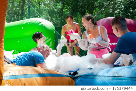 Joyful adults in inflatable pool with foam competing to collect balls 125379444