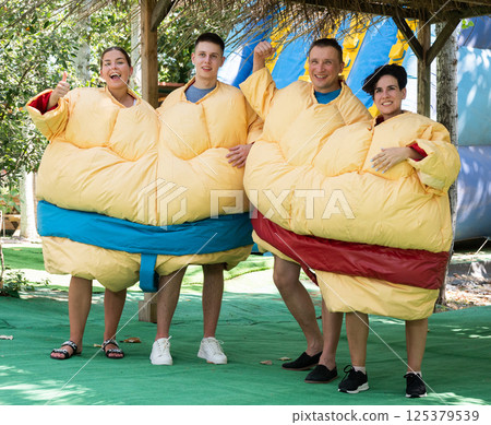 Cheerful friends posing in inflatable sumo twin suits in outdoor amusement park 125379539