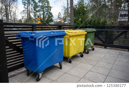 Three colored garbage bins for waste separation placed on outdoor pavement 125380177