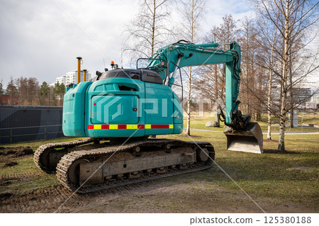 Large green excavator on grassy ground near construction site 125380188