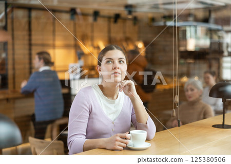 Relaxed young girl enjoying cup of coffee in cozy cafe Relaxed young girl enjoying cup of coffee in cozy cafe 125380506