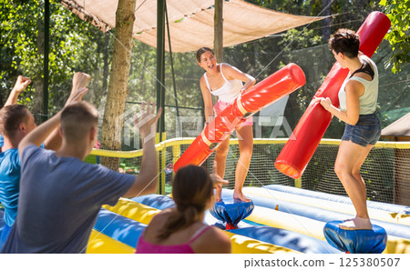 Women having pillow fight between each other in outdoor amusement park Women having pillow fight between each other in outdoor amusement park 125380507