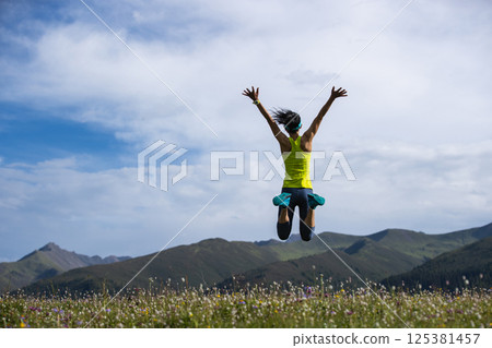 Cheering woman jumping at forest and grassland mountain top 125381457