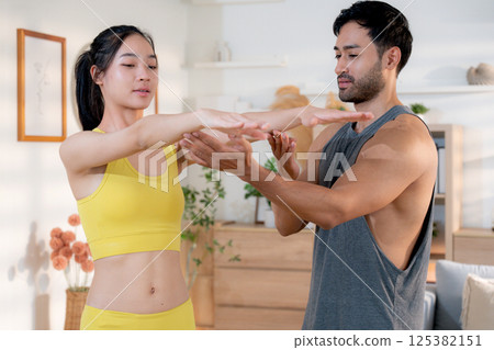 Fitness coach guidance with asian woman during squat training at home in living room. 125382151