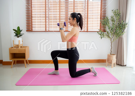 Young asian woman in sportswear workout with dumbbells for strength in living room. 125382186