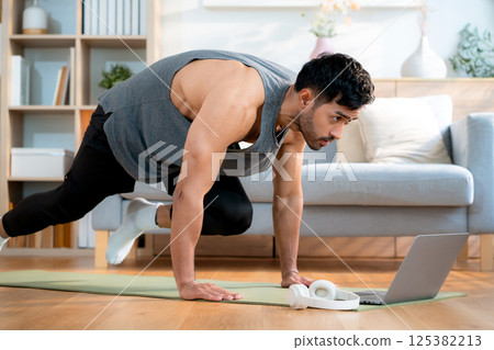 Young asian man doing home workout while watching online tutorial on laptop computer in living room. 125382213