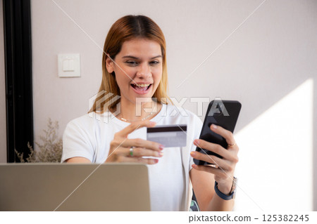 Happy young caucasian woman holding credit card or debit card paying with shopping online. 125382245