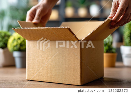 Hands opening cardboard box on wooden table indoors. Unboxing package 125382273