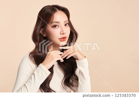 A beautiful young Asian woman with clean, fresh skin against a beige background. Skincare, facial treatment, cosmetology, beauty, and spa. An elegant portrait of an Asian woman. 125383370
