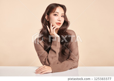 A beautiful young Asian woman with clean, fresh skin against a beige background. Skincare, facial treatment, cosmetology, beauty, and spa. An elegant portrait of an Asian woman. 125383377