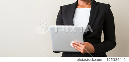African female adult professional holding tablet in black suit against neutral background 125384441